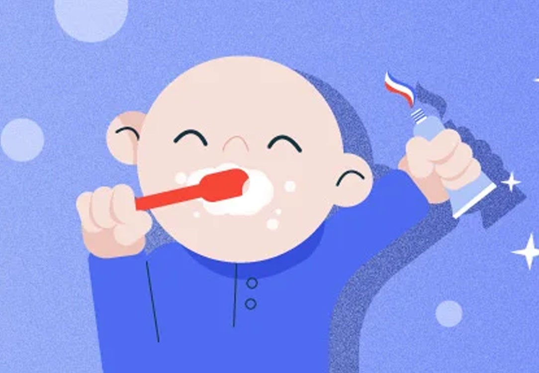 Toddler brushing his teeth with a tube of toothpaste in hand