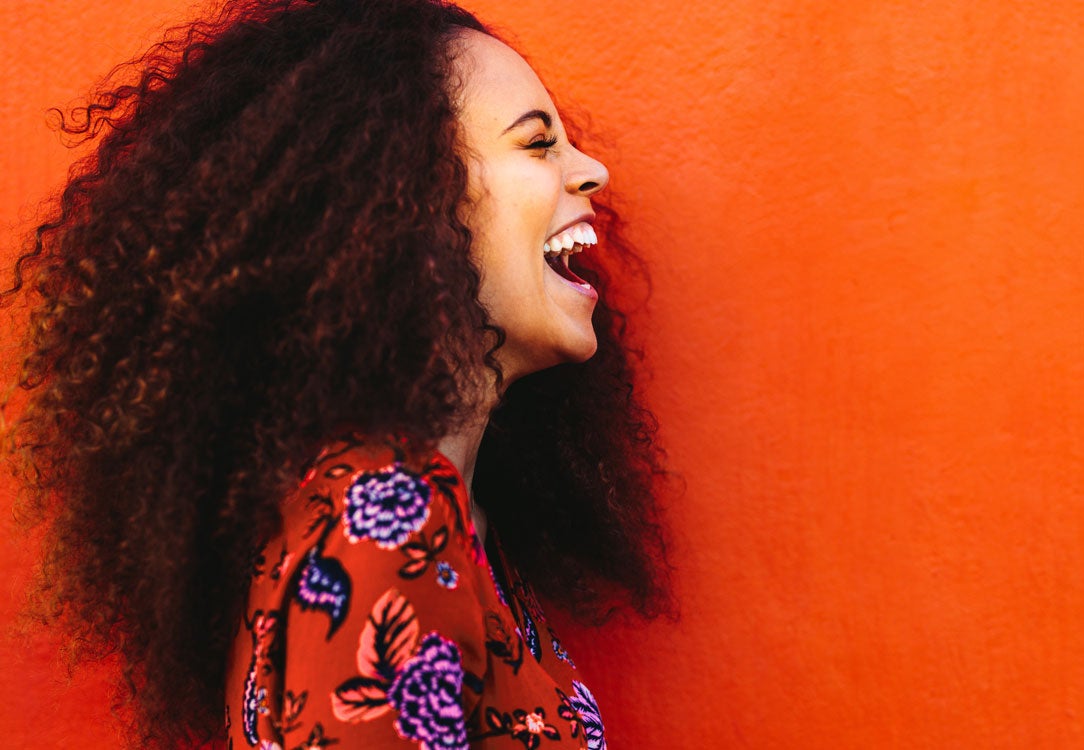 Stock image of side view of woman laughing in flower shirt on an orange background