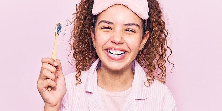 Girl with wavy hair holding up a pink toothbrush