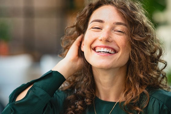 Young brunette woman laughing while touching her hair